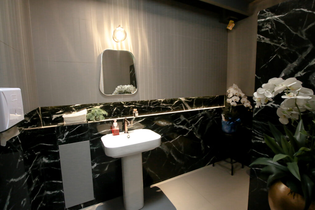 Blue Doors Cafe toilet with dark green white-veined marble walls, a white basin and a lit mirror