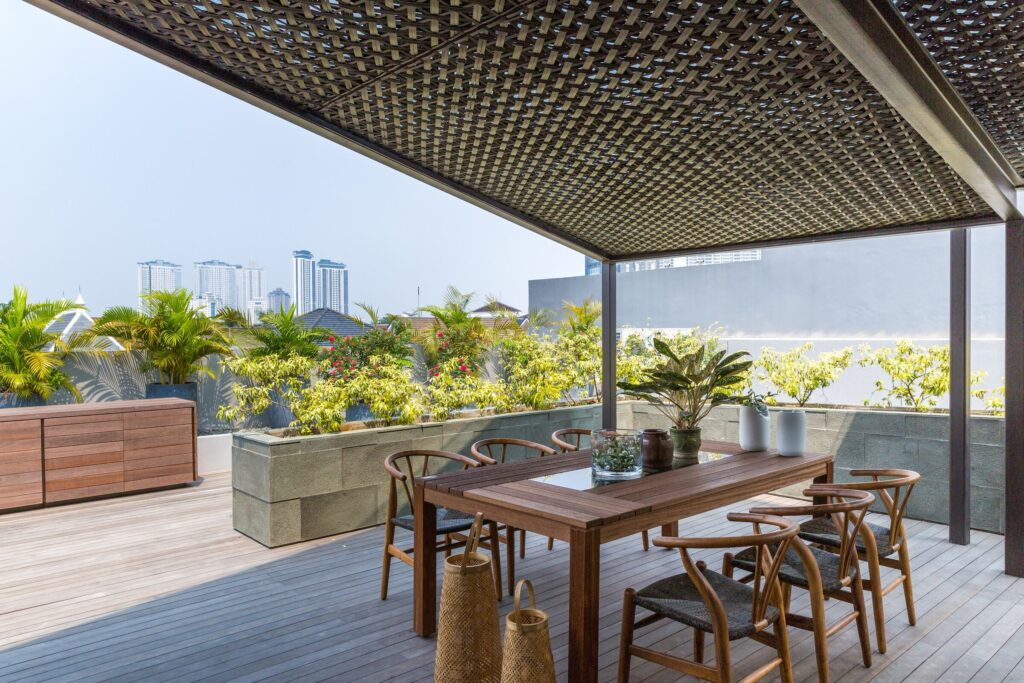 Weave House roof terrace with a wooden dining table under a lattice pergola, plants and city towers beyond