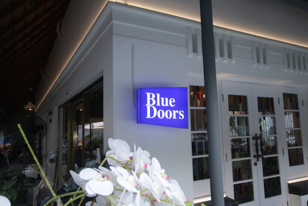 White facade of Blue Doors Cafe with a lit blue sign and heritage-style glass doors