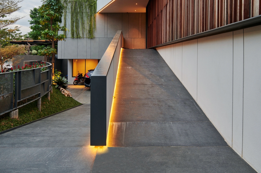 JE House ramp with a dark grey surface, a warm LED-lit parapet wall and a vertical timber-slat facade