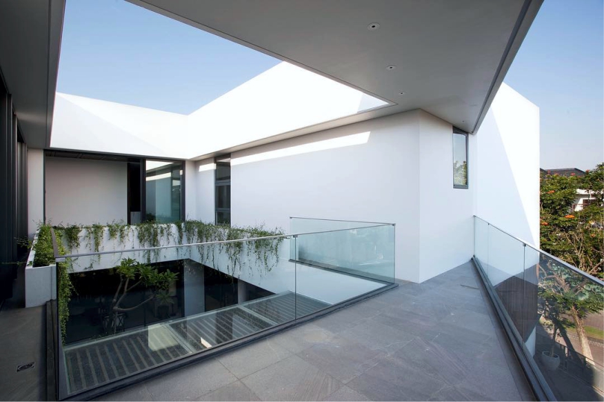 JE House upper terrace with a glass balustrade, a void open to the sky and trailing plants