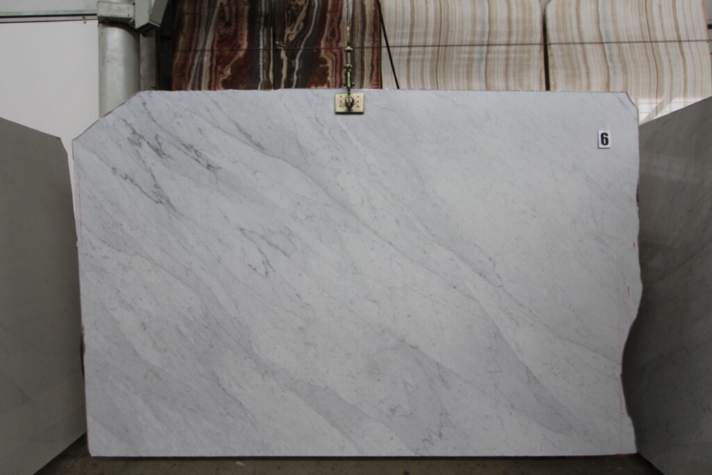 Carrara White marble slab with diagonal grey veins, hanging in a warehouse