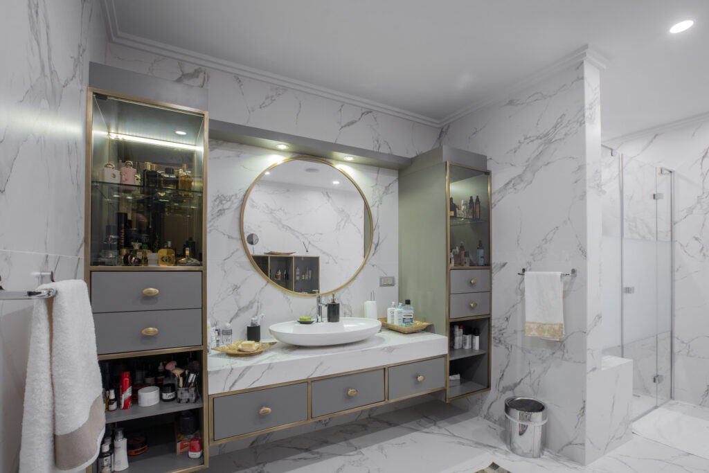 Bathroom with white grey-veined Dekton Aura walls and floor, a round mirror and grey cabinets