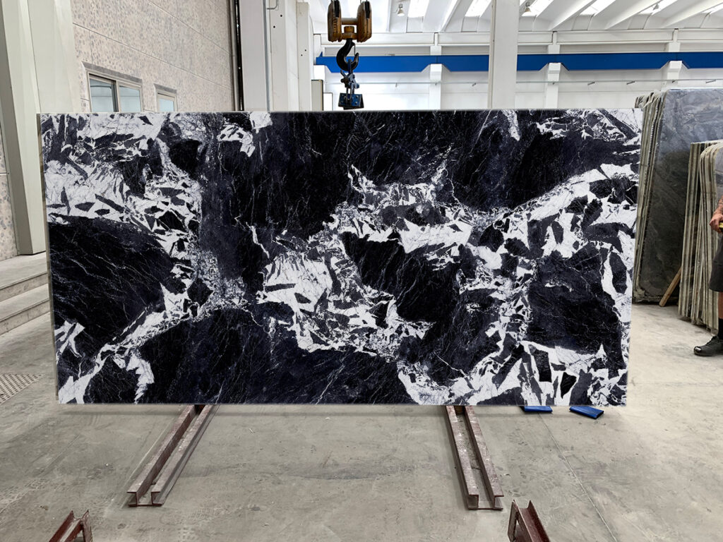 Mediterraneo Noir Grand Antique slab, black with a large contrasting white pattern, standing on a warehouse rack