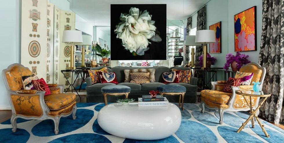 Bohemian living room with ornate orange armchairs, a round white coffee table, a blue patterned rug and bold artwork