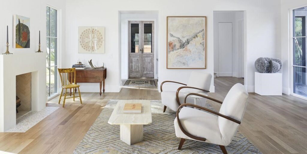 Minimalist white living room with pale wood floors, a low coffee table, curved armchairs and a fireplace