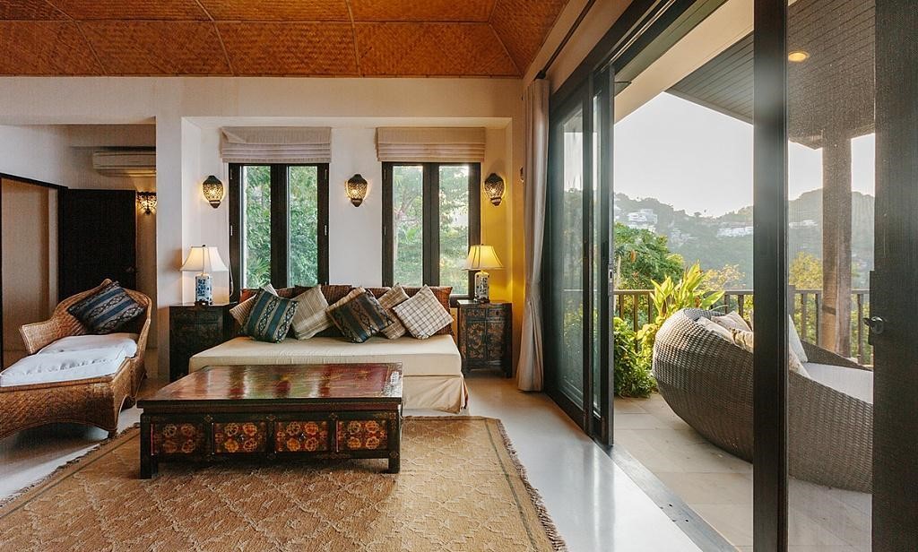 Tropical living room with a woven rattan ceiling, carved wooden coffee table and glass doors open to a jungle view