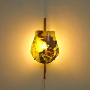 Kantung Semar wall lamp in Golden Green onyx, glowing warm yellow against a wall