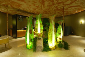Kantung Semar standing lamps in Golden Green onyx, glowing from within, grouped among ferns